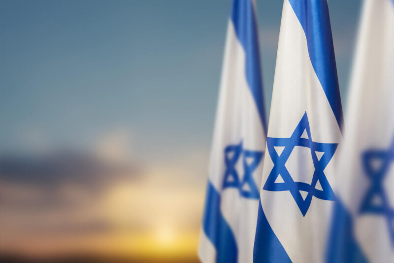 En rekke med israelske flagg mot en himmel der solen går ned.